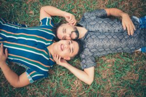Two men laying down with their heads together, learning how to listen to each other. They are supported by a couples therapist in Manhattan.