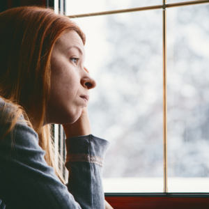 A woman looking out the window at snow displaying depression symptoms. If you are suffering with the winter blues like her out Brooklyn depression therapists can help.