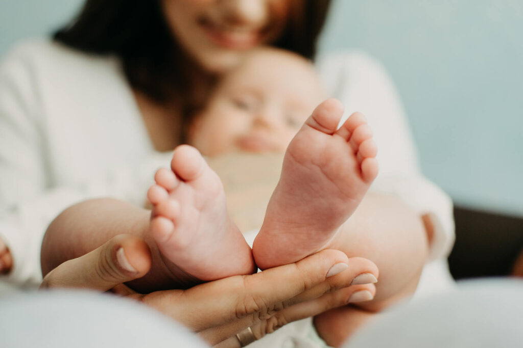 A mom holding up the feet of her baby. Representing how much better you can feel after talking to a postpartum depression therapist about your maternal mental health in Manhattan.