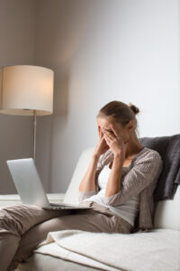 A woman with her head in her hands looking down at a laptop. Representing someone who could benefit from therapy or counseling for women in Manhattan or Brooklyn. If you are struggling like the woman in the image our female therapists in New York can help.