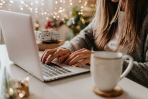 A woman typing on a laptop in front of twinkle lights in Brooklyn, New York. Representing someone who is meeting with a depression therapist from their apartment. Online & in-person depression therapy can help relieve you SAD symptoms.