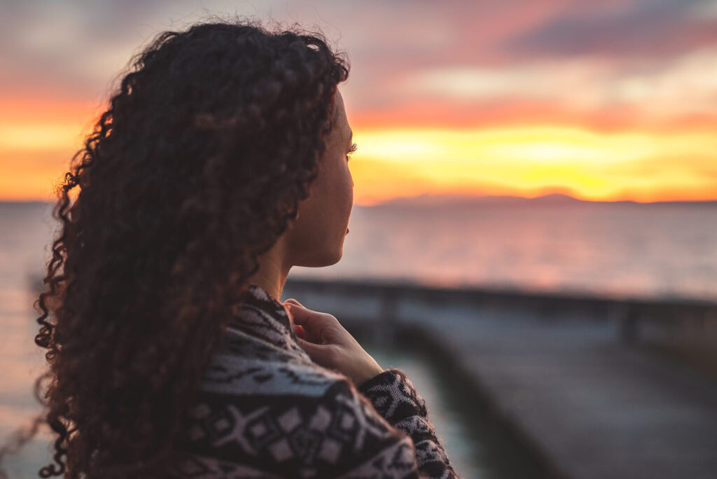 A woman with curly hair looking at the sunset in New York. Showing someone who is learning how to balance her perspective with CBT for anxiety in Manhattan. Learn techniques from a therapist & start enjoying your life with anxiety counseling.
