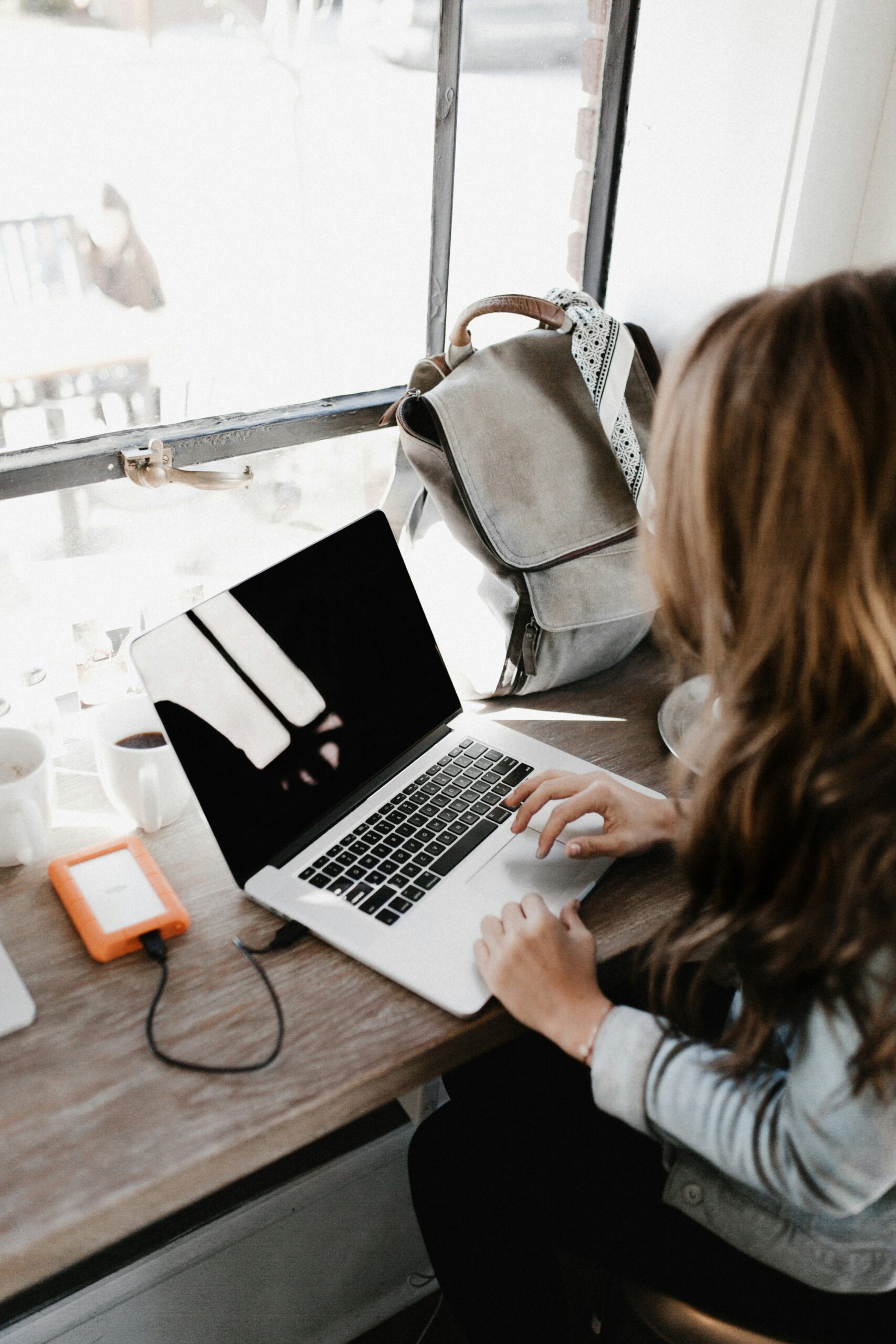 Working mom on laptop at a coffee shop with her baby backpack on the table. 8 tips to help working Manhattan moms balance career and motherhood in New York.