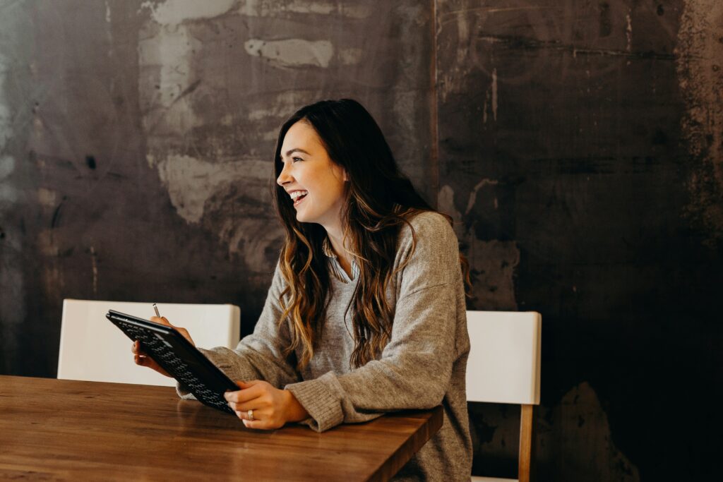 Woman sitting in a meeting in Brooklyn, smiling and using her Ipad. Is it time to leave your job? Find out how to spot the signs with therapists tips and tricks. 