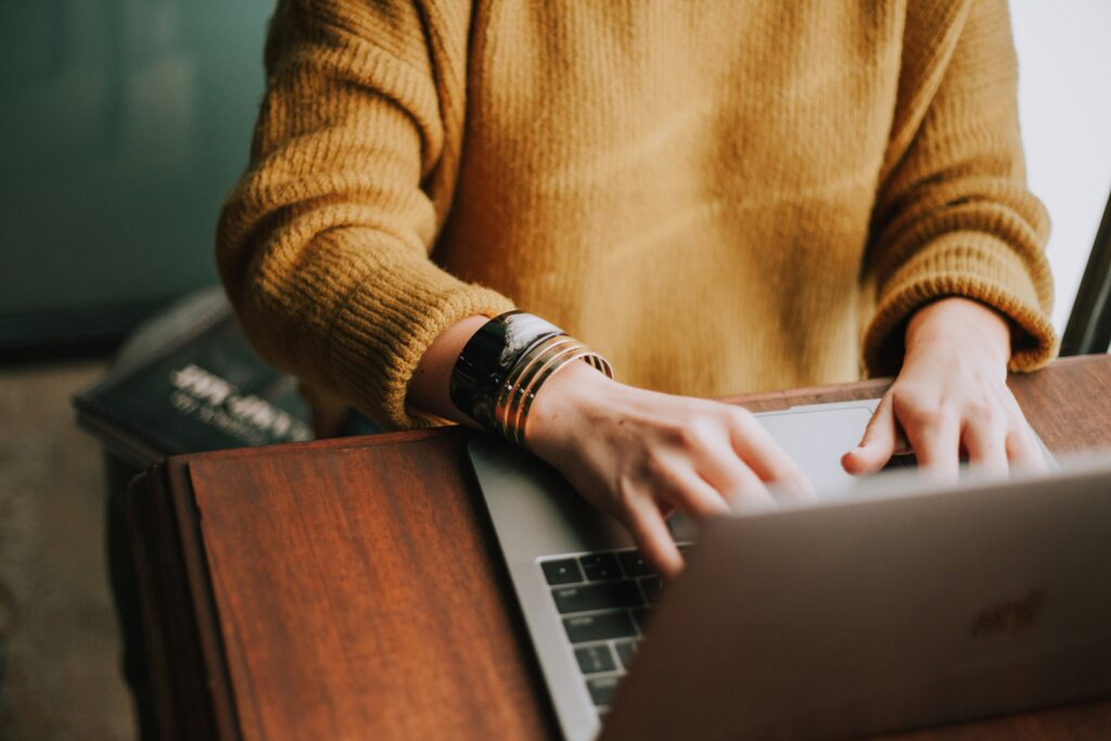 Woman in a yellow sweater with gold bracelets typing on her computer. Find out if tips on if you should leave your Manhattan job. 
