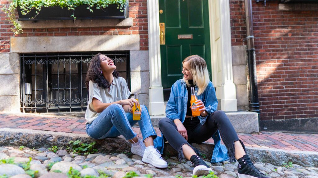Two women sitting on a Brooklyn street drinking sodas and laughing. Going to therapy for the first time can be scary. Learn more about what you can expect with our Brooklyn therapists tips and tricks. 