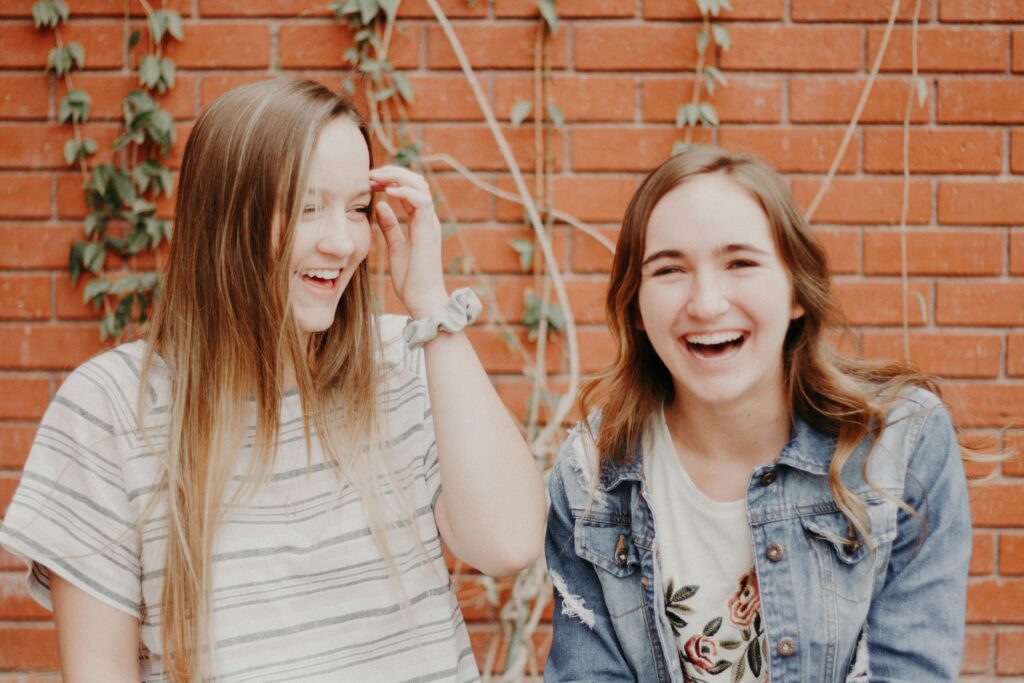 two woman laughing in front of a brick wall in Brooklyn. including your support system in your eating disorder recovery is key.