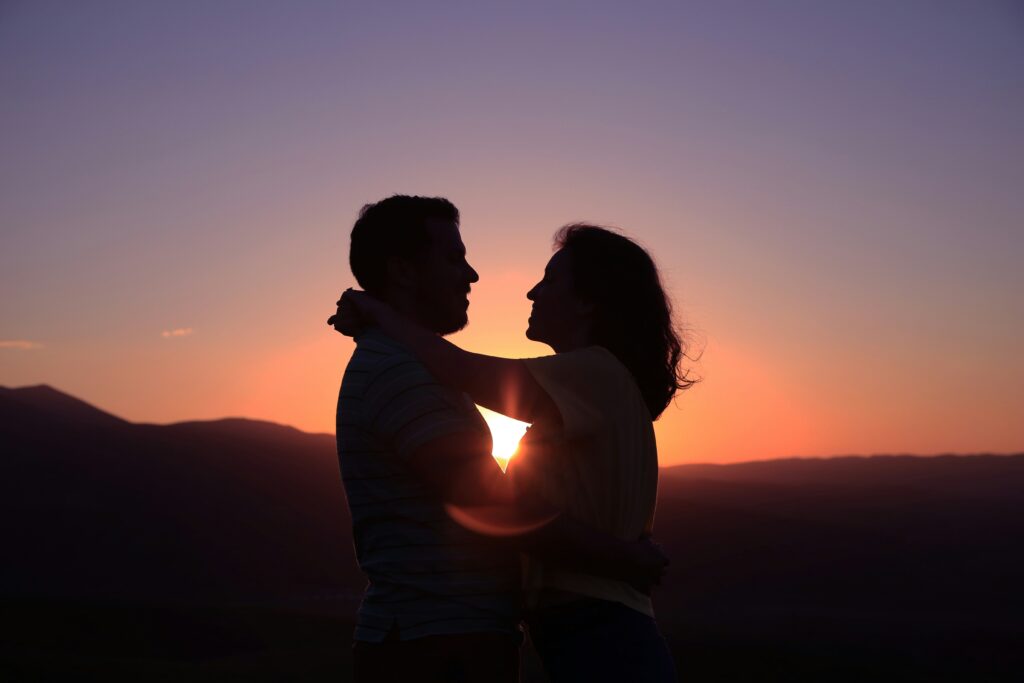 Couple standing in the mountains, hugging and backlit by the sunset. Communication is a huge part of sexual attraction, even when you don't have it from the start. 