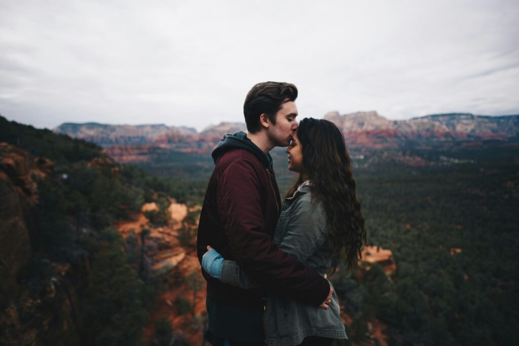Man kissing forehead of his partner on top of a cliff overlooking a valley. Relationships must be consistent and based on values. It's more than just liking someone. 