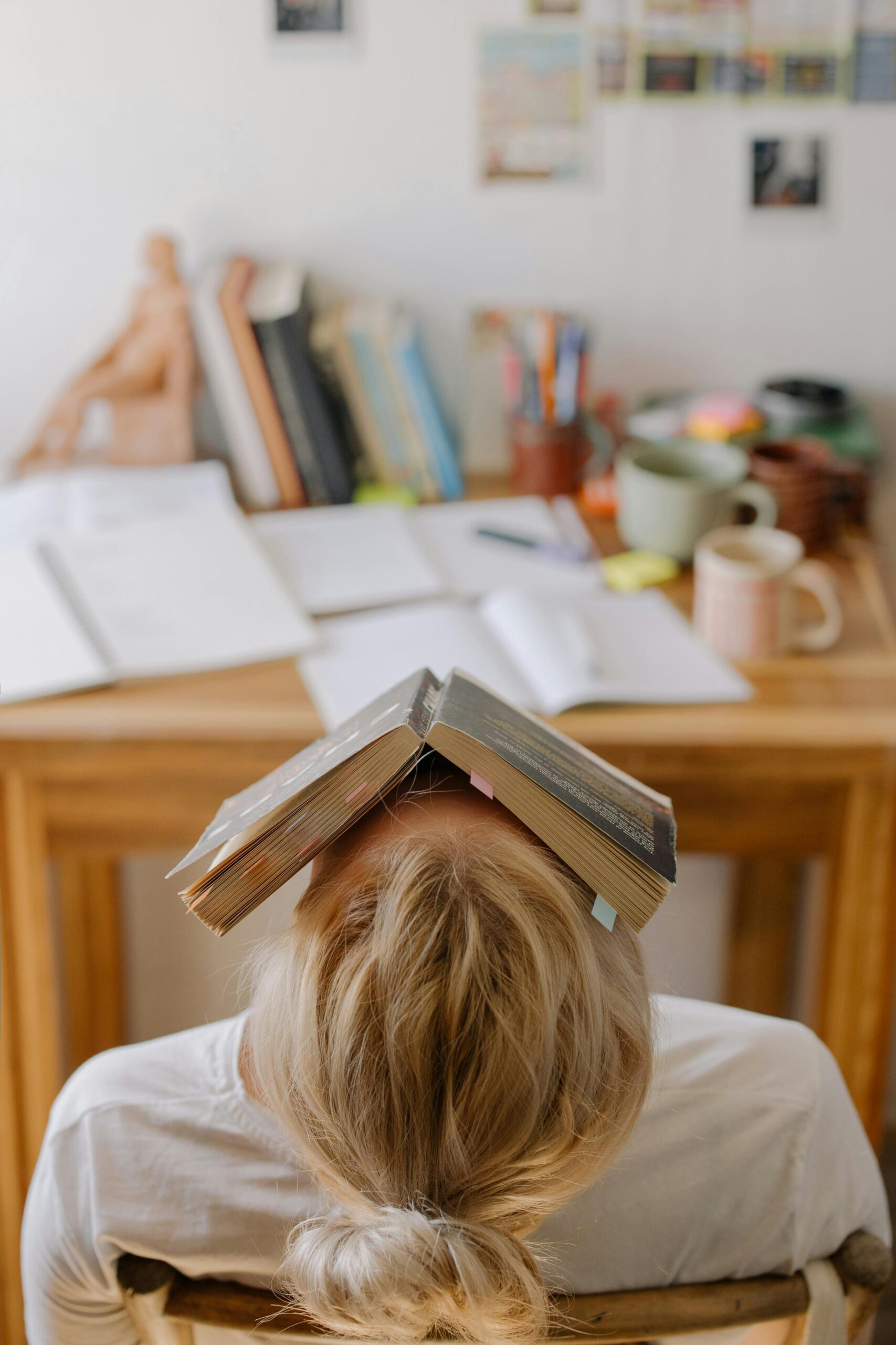 New York City woman sitting at her desk after a stressful day, with a book on her face, leaning backwards. Time management can help you feel less stressed in the day to day.