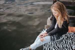 A Manhattan woman sitting on a dock, breathing and trying to reconnect with the world around her. Emotional numbness happens, but with therapy, you can find new strategies to overcome.