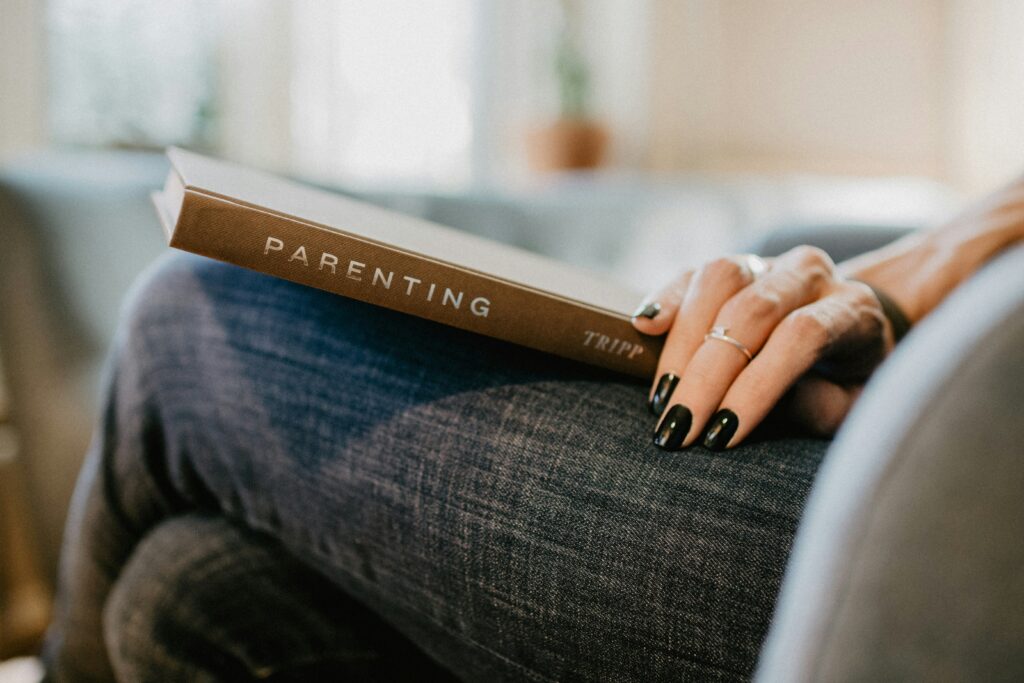 woman sitting on a couch reading a parenting book. Your fertility journey may be hard, but therapy in Brooklyn can help you though it. 