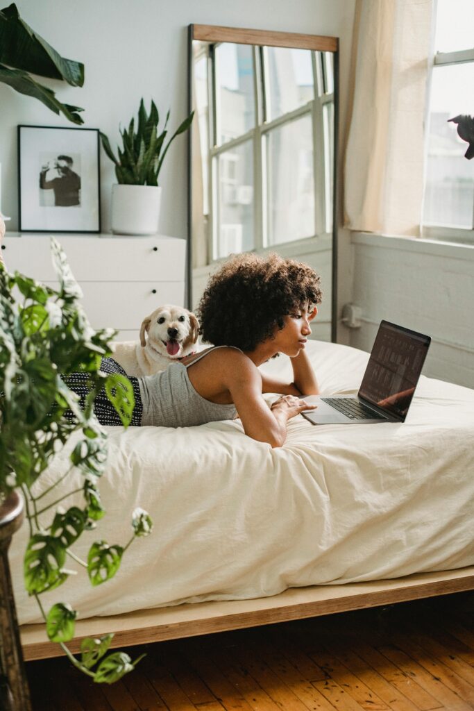 New York City woman laying on her bed working on her computer. Time management tips can help you manage stress levels. 