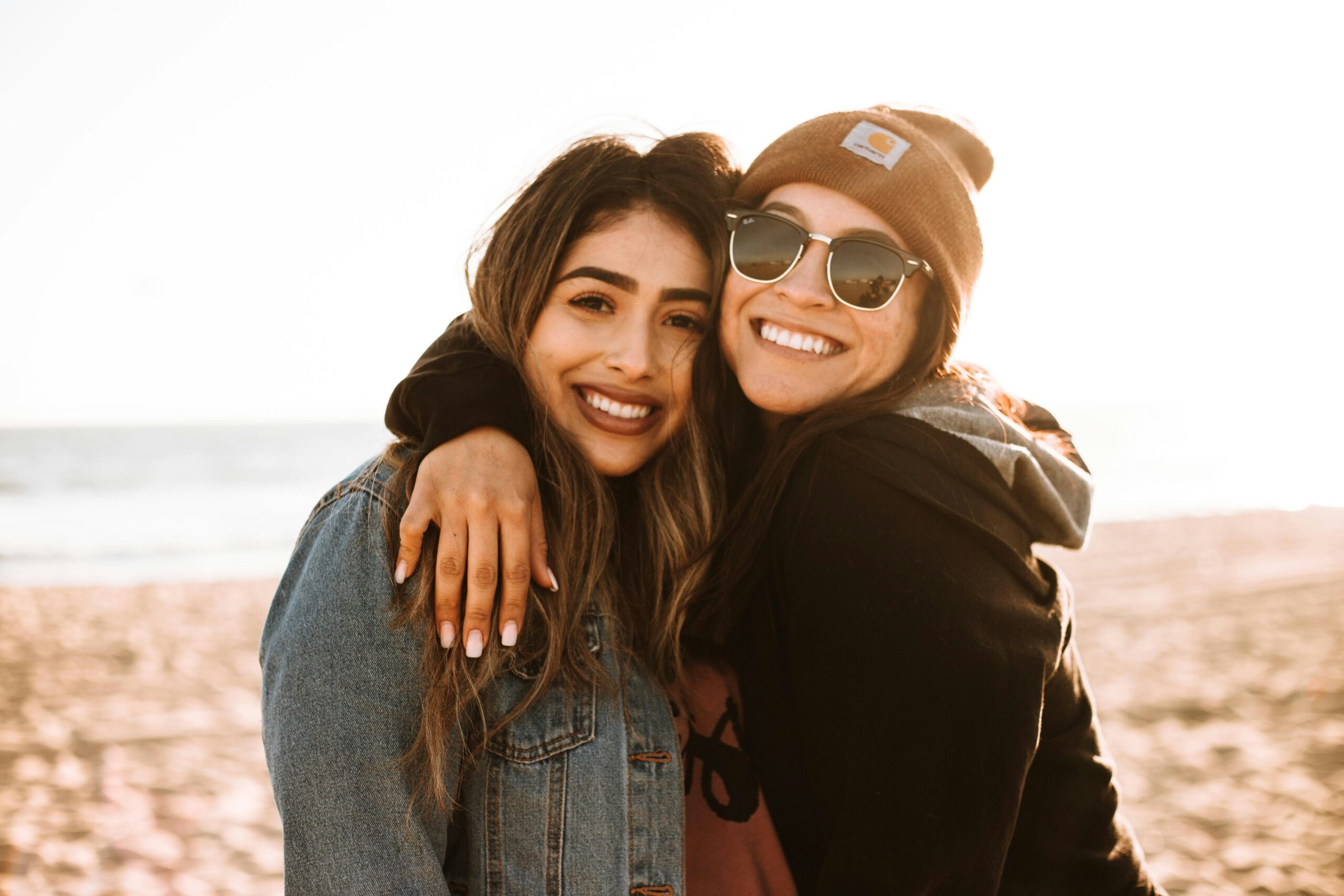 Two women on a beach in Manhattan, smiling and hugging each other. Understanding self esteem can help you grow.