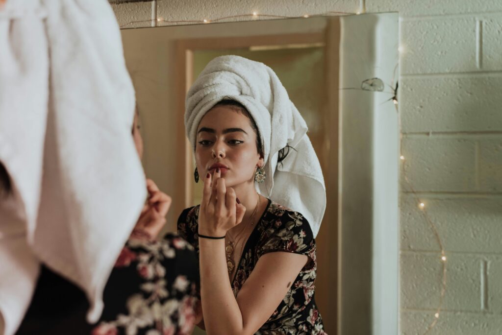 Manhattan woman putting on her makeup, looking in the mirror, with her hair in a towel. Negative inner voice can overwhelm your life, but with Manhattan Wellness therapists, you can learn how to quiet them. 