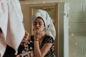 Manhattan woman putting on her makeup, looking in the mirror, with her hair in a towel. Negative inner voice can overwhelm your life, but with Manhattan Wellness therapists, you can learn how to quiet them.