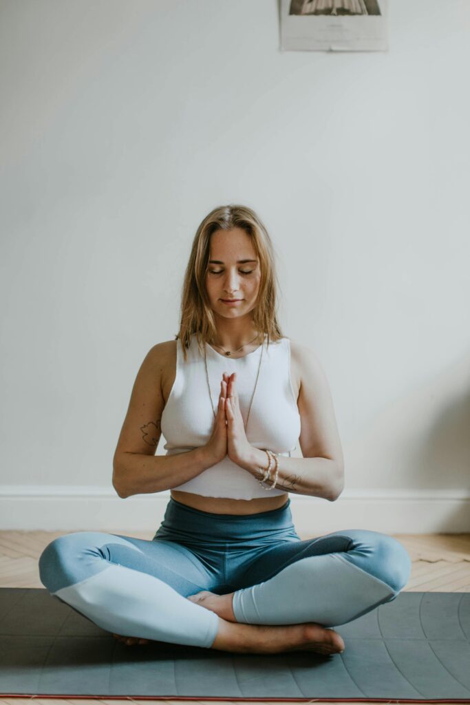 Woman in a yoga pose, sitting on the floor in her Brooklyn apartment. Overcoming your negative inner voice is possible with these tips from Manhattan Wellness. 
