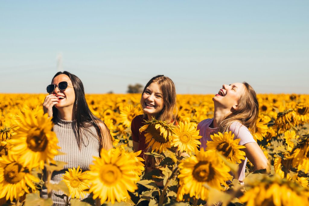 Three NYC friends laughing and playing a sunflower field. Negative self talk can impact our moods, so focus on improving your negative self talk with therapy. 