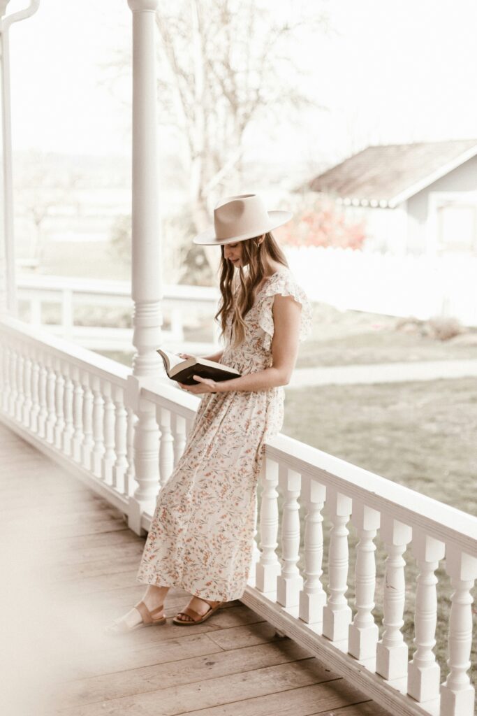 New York City woman sitting on a porch rail reading book and practicing limiting her negative self talk.