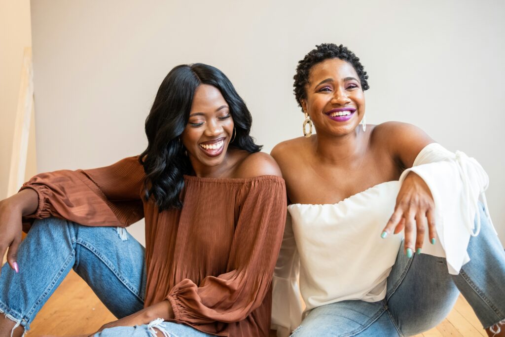 Two New York City women sitting together and smiling. Negative self talk can really impact your moods. 