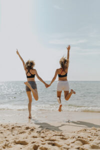 Two friends on a beach, jumping for a picture. College can bring on comparison. Therapy can help you overcome.