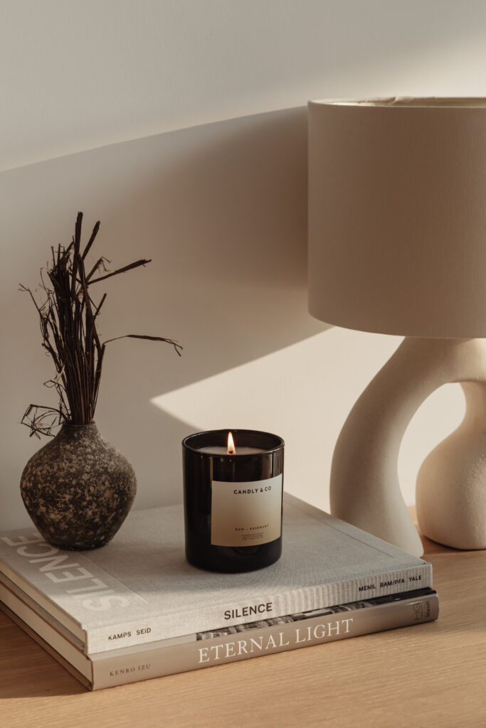 Calming lit candle on a table next to a lamp, on top of books.