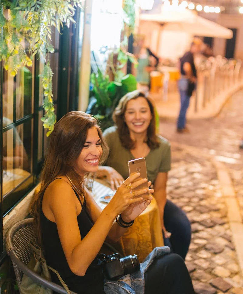 Two women smiling taking a picture on phone at dinner table.