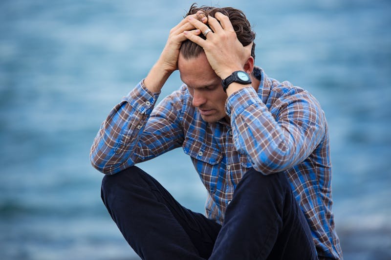 New York City man sitting on the ground, his hands in his hair. Depression is hard, therapy can help. 