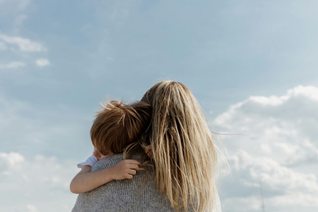 Mom holding son sleeping on her shoulder under the blue sky.