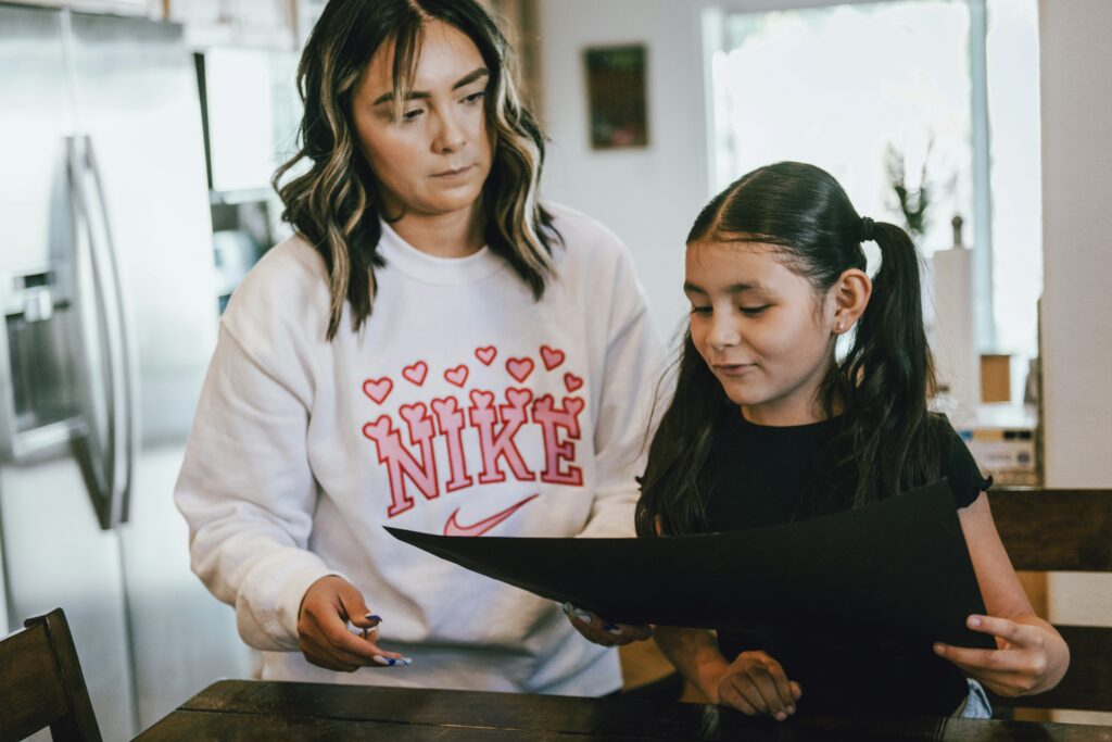 Mom helping her child with homework, not smiling, both looking at what daughter is holding.