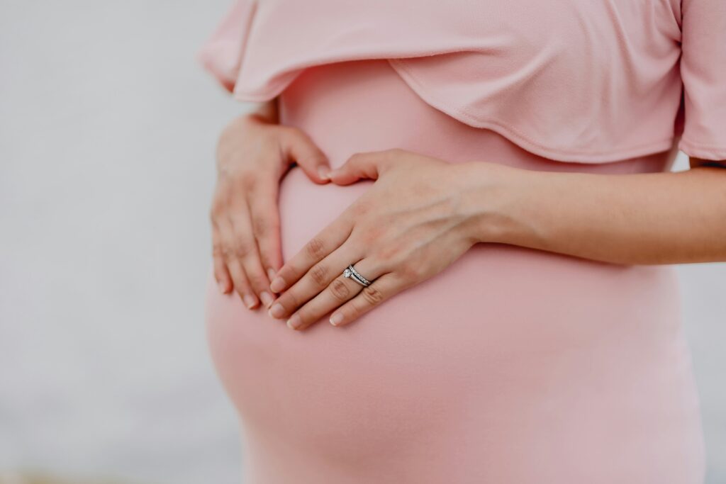 Pregnant woman in pink dress holding her stomach.