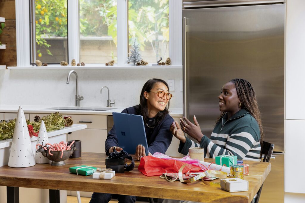 Two women smiling together in a kitchen on a computer.