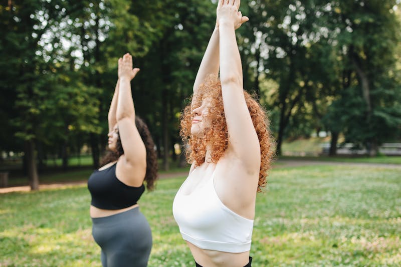 Two women doing yoga outside in the grass.