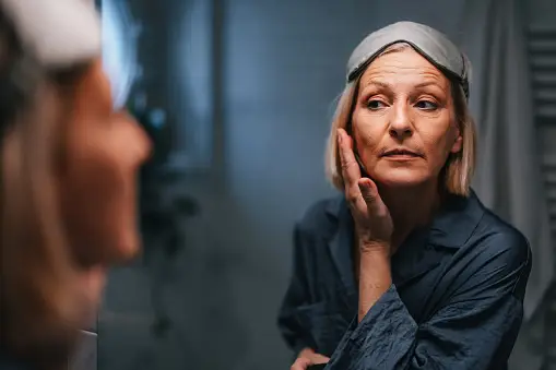 Woman looking at herself in the mirror, touching her face.