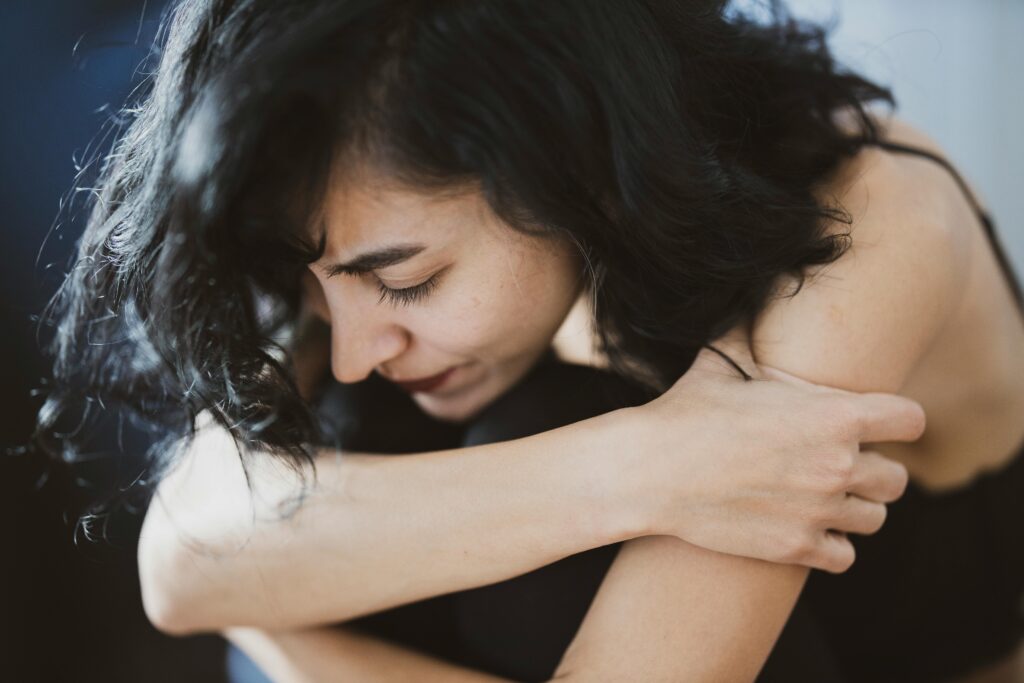 Close up image of a woman hugging her knees in close to her body.