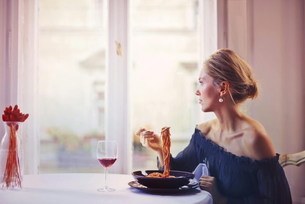 Woman eating pasta and drinking wine at the table.