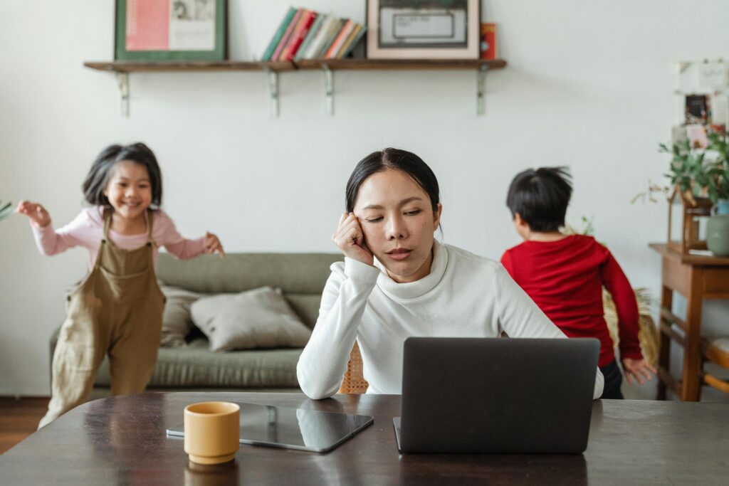 Stressed mother on her computer with kids running around behind her.