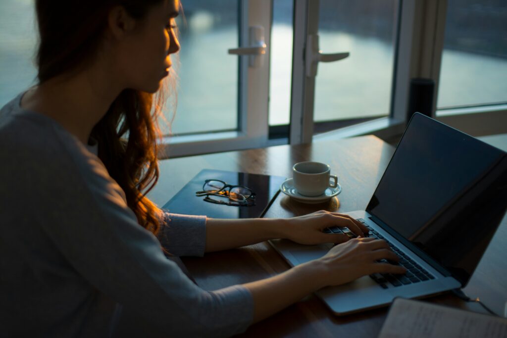 Woman on her computer with coffee and glasses on table.