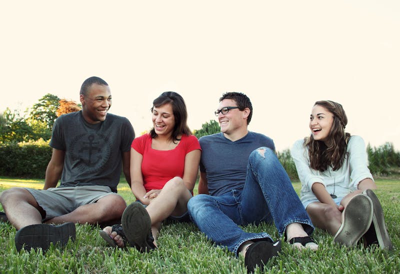 Friends sitting in grass laughing together.