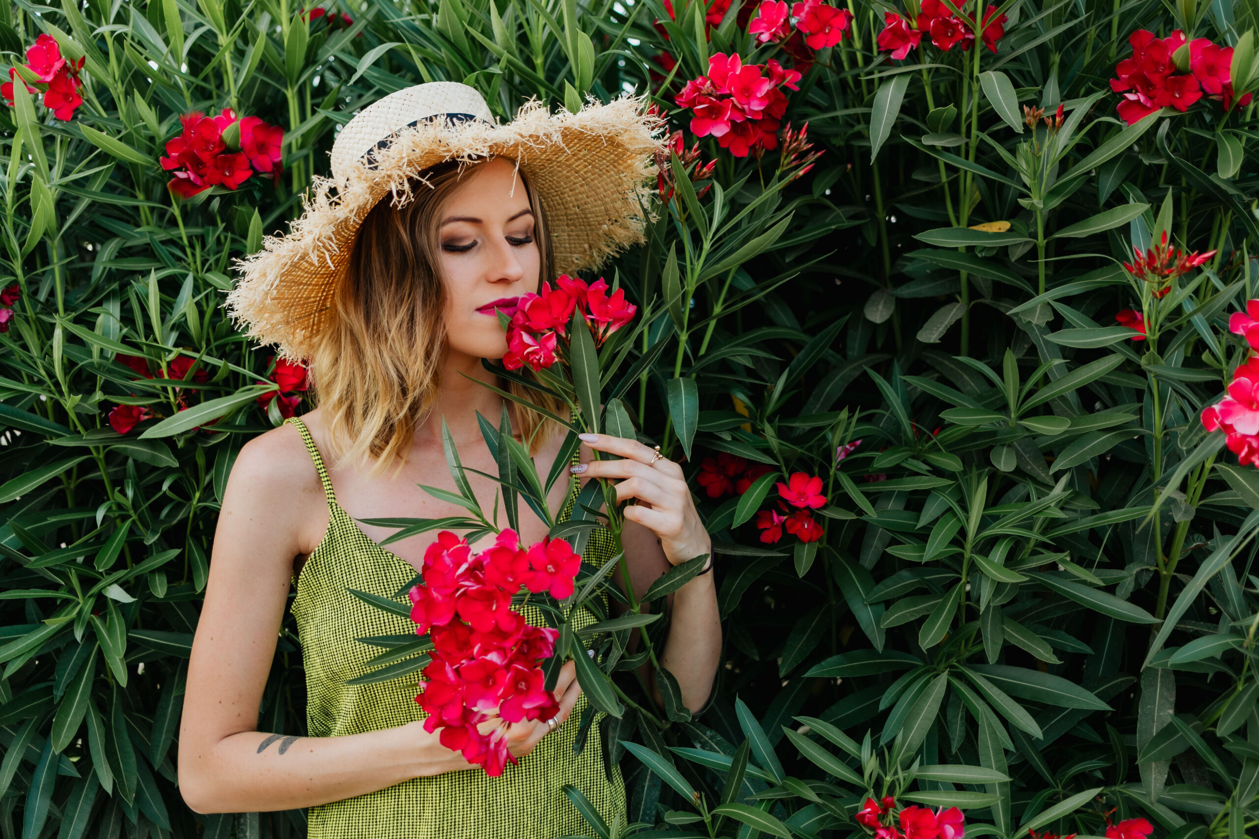 Woman smelling the pink flowers in a straw hat.