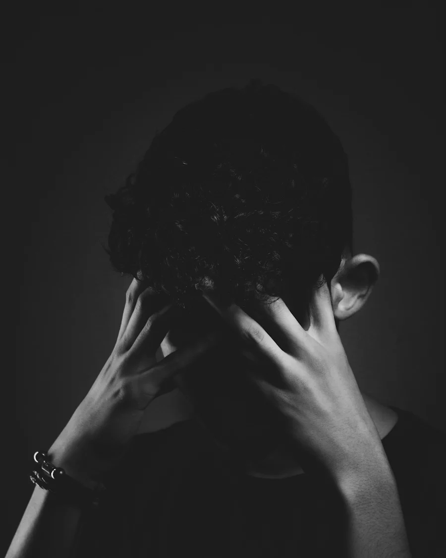 Black and white picture of a persons hands over their face.