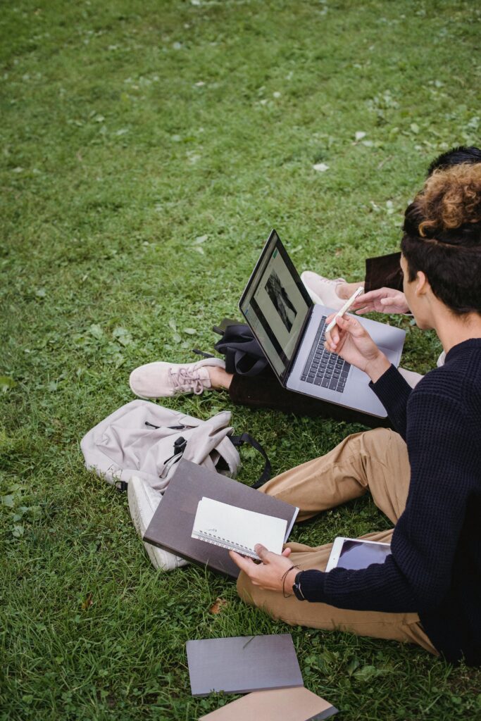 Friends sitting outside together doing work on the grass.