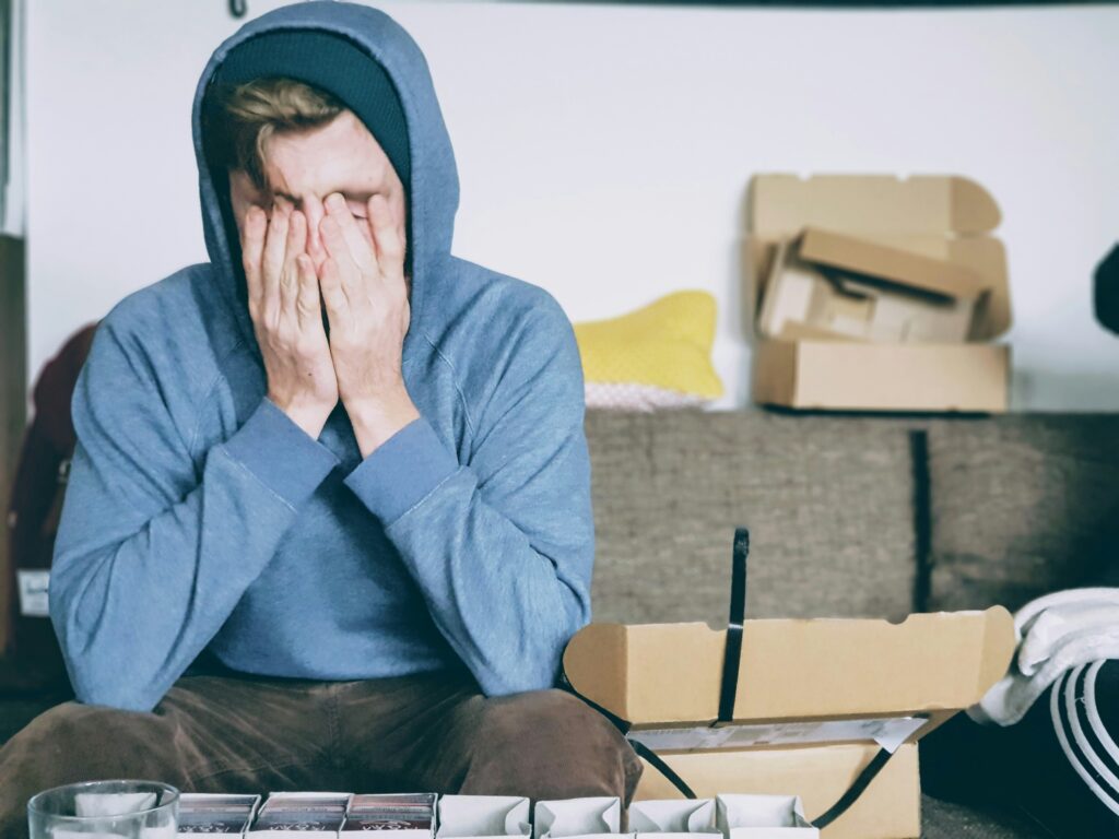 Man with his hood on and hands covering his eyes.
