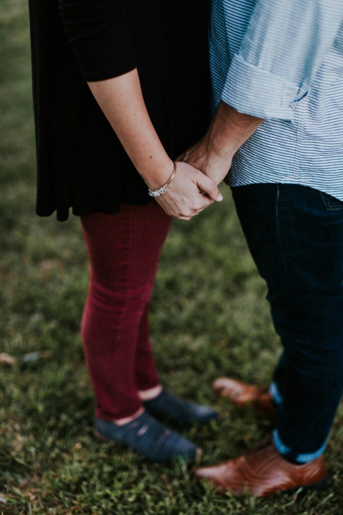 Couple holding hands facing each other in the grass.