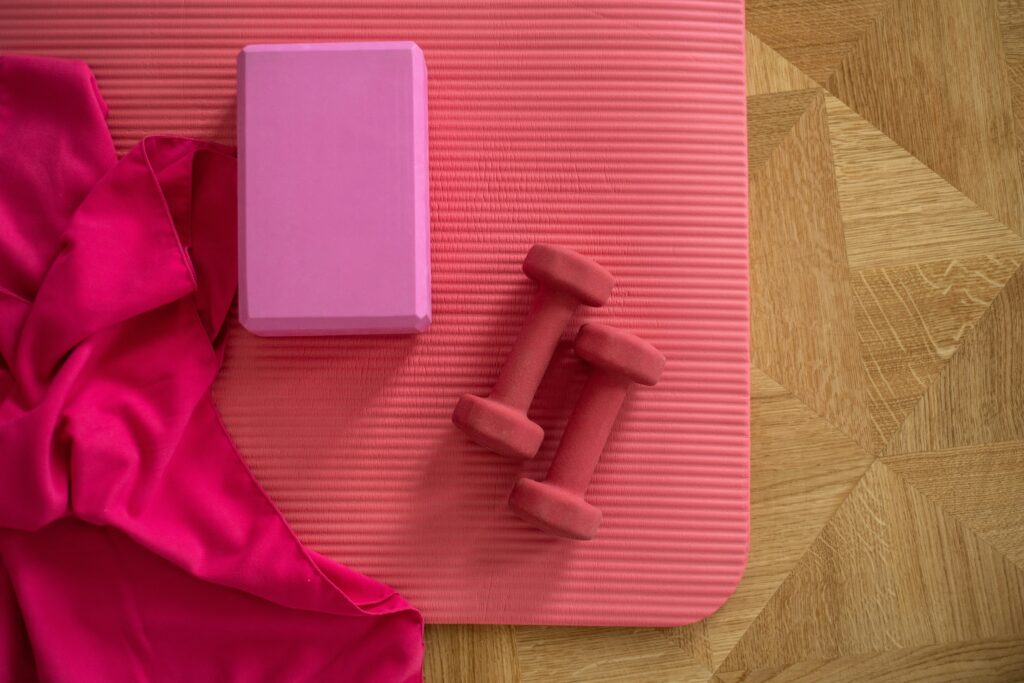 All pink weights, and block, and towel on yoga mat.