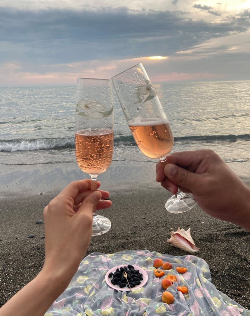 Couple doing champagne toast on the beach with picnic.