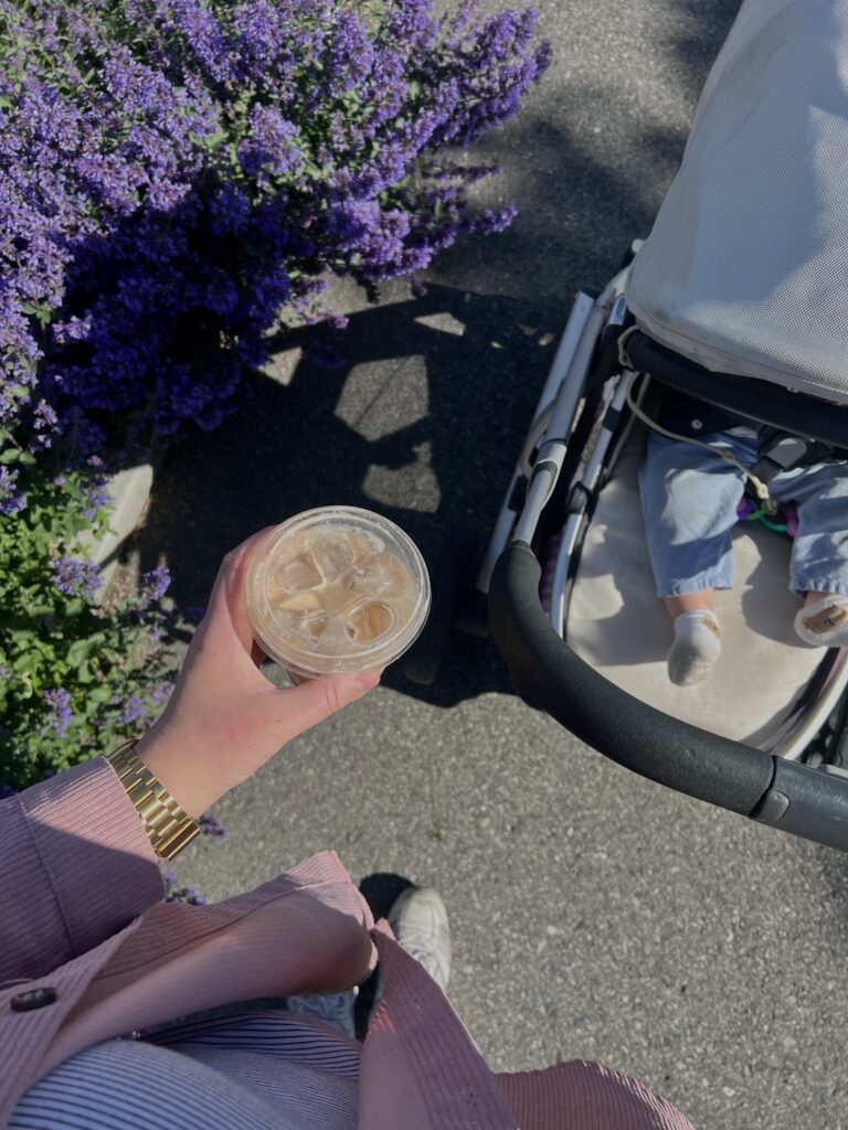 Mom walking baby in stroller with coffee in her hand.