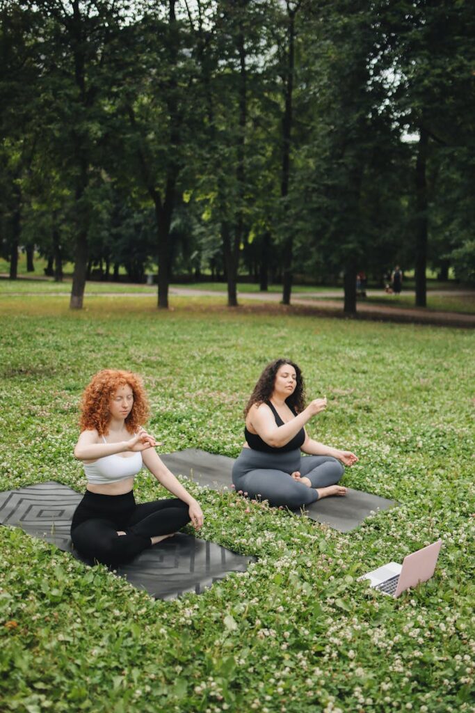 Two women doing meditation in the grass outside.