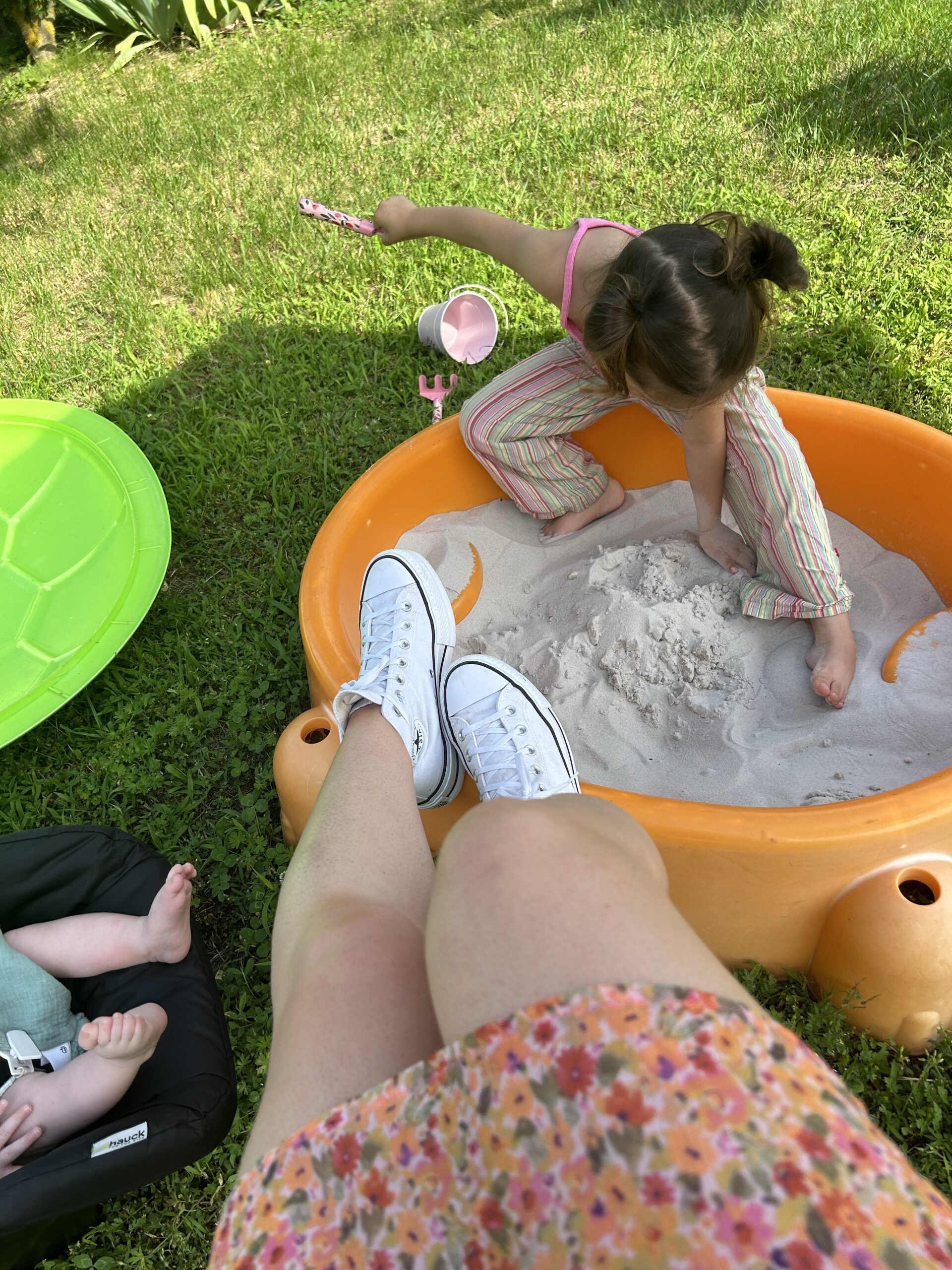 Child playing in sandbox and mom sitting watching.