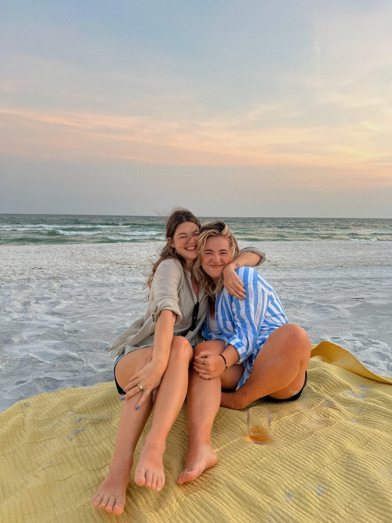 Friends smiling on the beach on a blanket together.